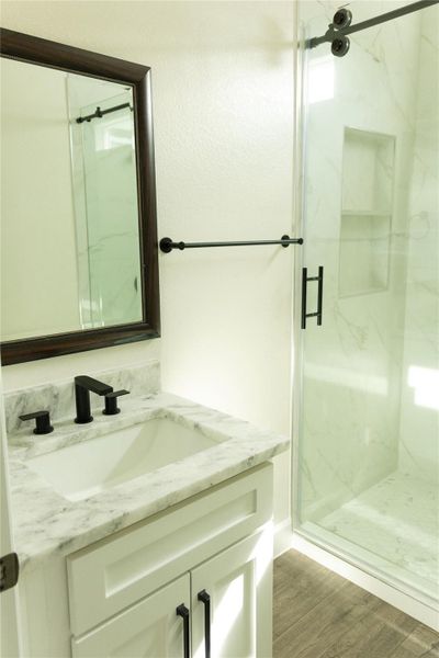 Full bathroom featuring vanity, a marble finish shower, and light wood-type flooring