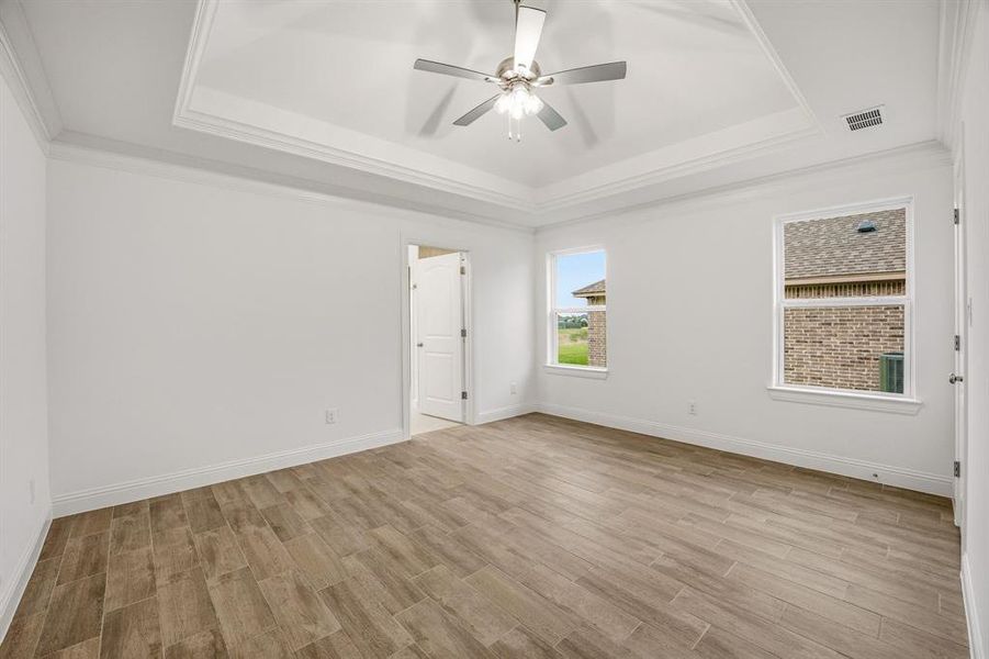 This room features light wood-look flooring, a tray ceiling, and a ceiling fan with integrated lighting