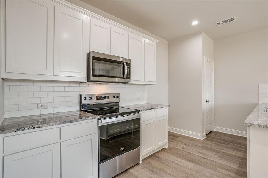 Kitchen with stainless steel appliances, white cabinetry, light stone counters, decorative backsplash, and light wood finished floors