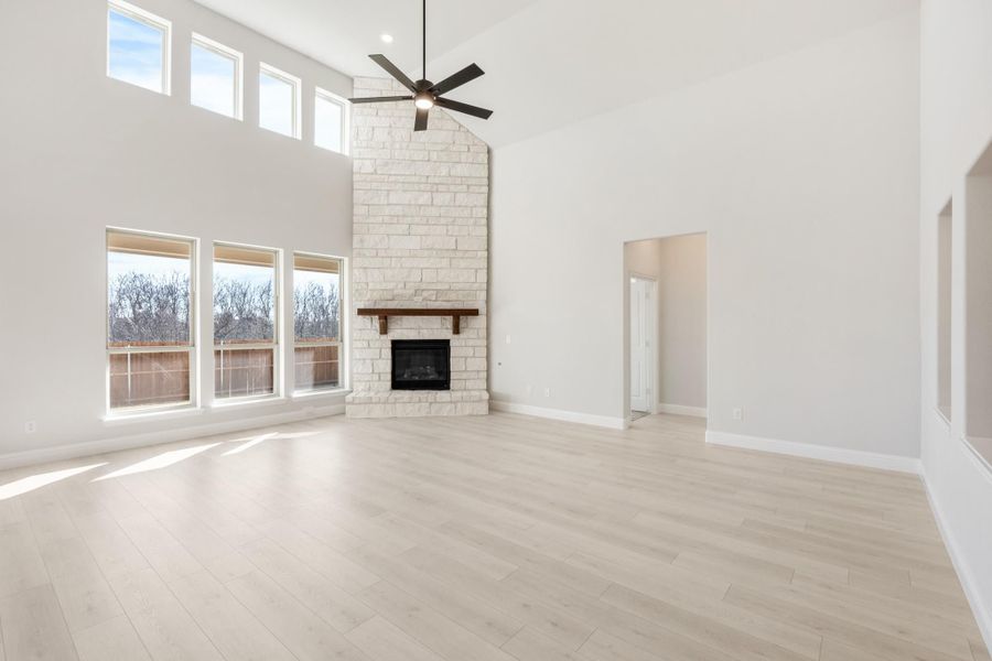 Open living room with vaulted ceiling, floor-to-ceiling stone fireplace, ceiling fan, and light hardwood floors