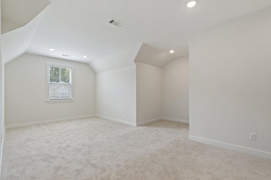 Spacious room featuring vaulted ceilings, recessed lighting, neutral carpet flooring, and a single window with blinds