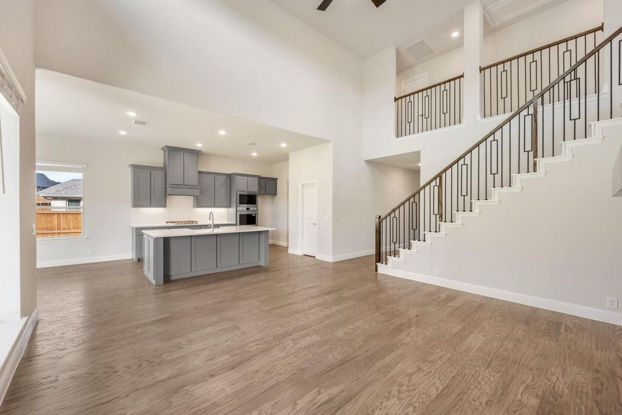 Open-concept living area with hardwood floors, gray kitchen island, and two-story staircase with iron balusters Open-concept living area with hardwood floors, gray kitchen island, and two-story staircase with iron balusters
