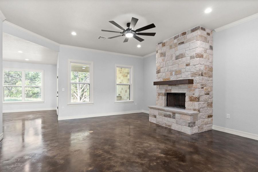 Unfurnished living room featuring ornamental molding, finished concrete floors, a stone fireplace, a ceiling fan, and recessed lighting