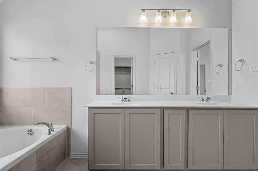 Full bathroom featuring double vanity, a bath, and a spacious closet Full bathroom featuring double vanity, a bath, and a spacious closet