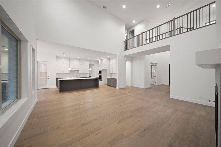 Unfurnished living room featuring light wood-type flooring, recessed lighting, and a towering ceiling