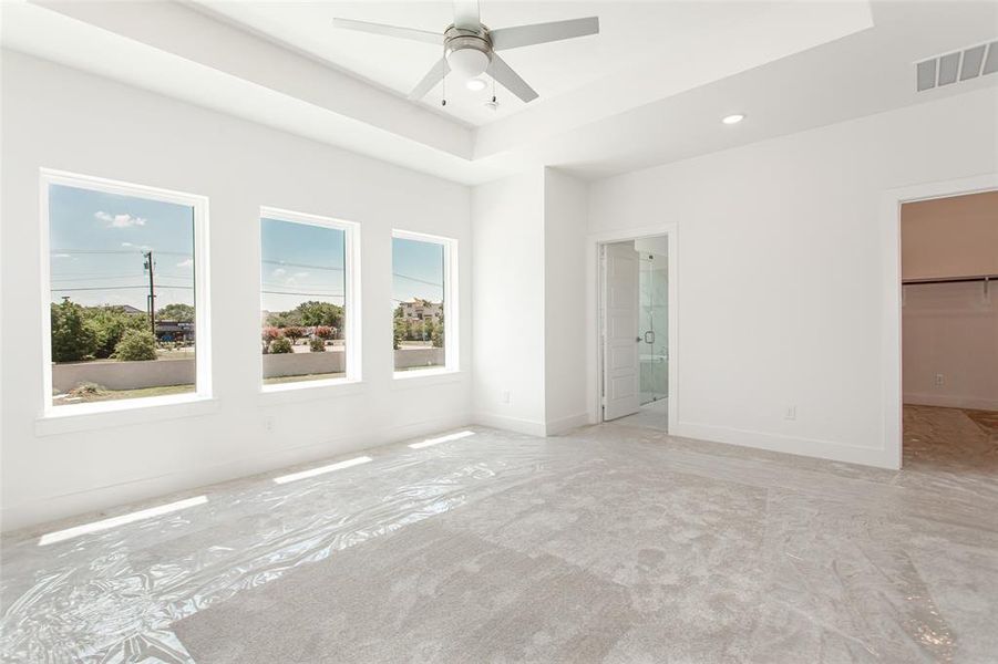 Unfurnished bedroom featuring connected bathroom, ceiling fan, a raised ceiling, and a walk in closet