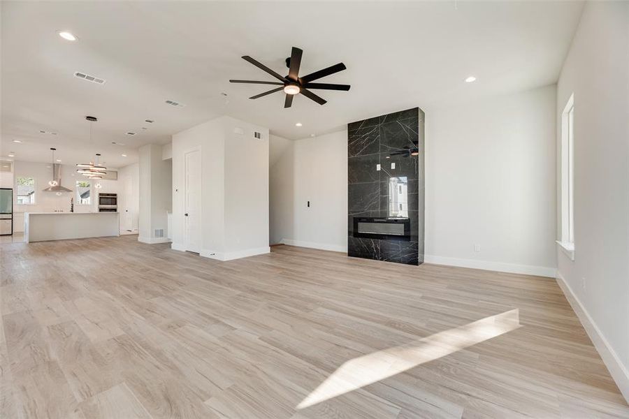 Unfurnished living room with light wood-style flooring, ceiling fan, a premium fireplace, and recessed lighting Unfurnished living room with light wood-style flooring, ceiling fan, a premium fireplace, and recessed lighting