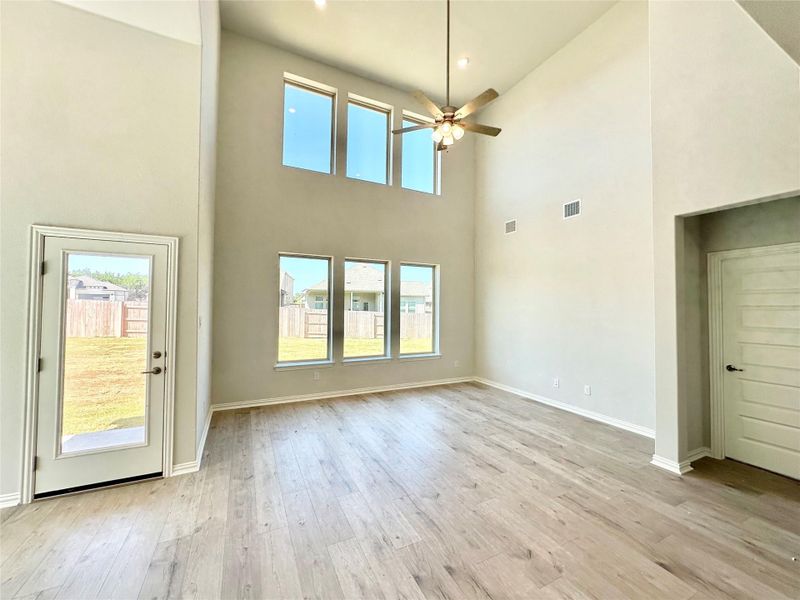 Unfurnished living room with light wood-style flooring, ceiling fan, and a towering ceiling Unfurnished living room with light wood-style flooring, ceiling fan, and a towering ceiling