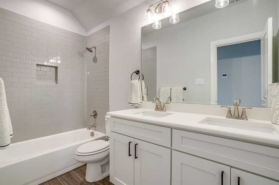 Bathroom with double vanity, shower / washtub combination, dark wood-type flooring, and vaulted ceiling