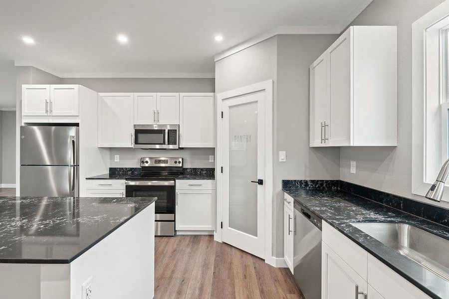 Kitchen with dark stone counters, appliances with stainless steel finishes, white cabinets, ornamental molding, and light wood-style flooring