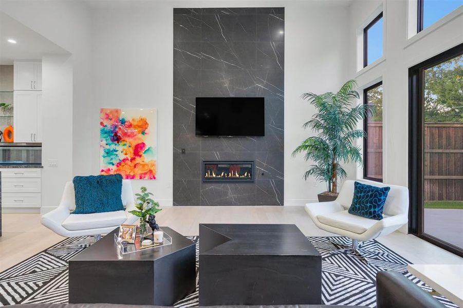 Living room featuring light wood-style flooring, a fireplace, and a high ceiling Living room featuring light wood-style flooring, a fireplace, and a high ceiling