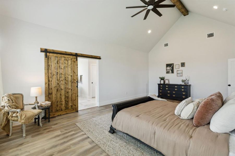 Vaulted ceiling with exposed wood beam, wood-finish flooring, recessed lighting, and a dark wood barn door on a black rail