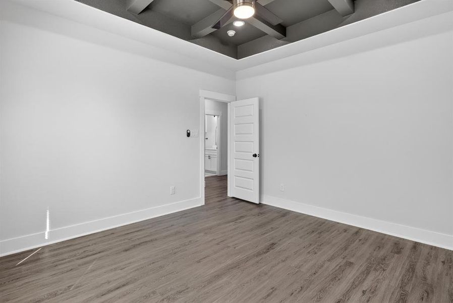 Spacious interior room featuring wood-finish flooring, white baseboards, and a tray ceiling with a dark finish