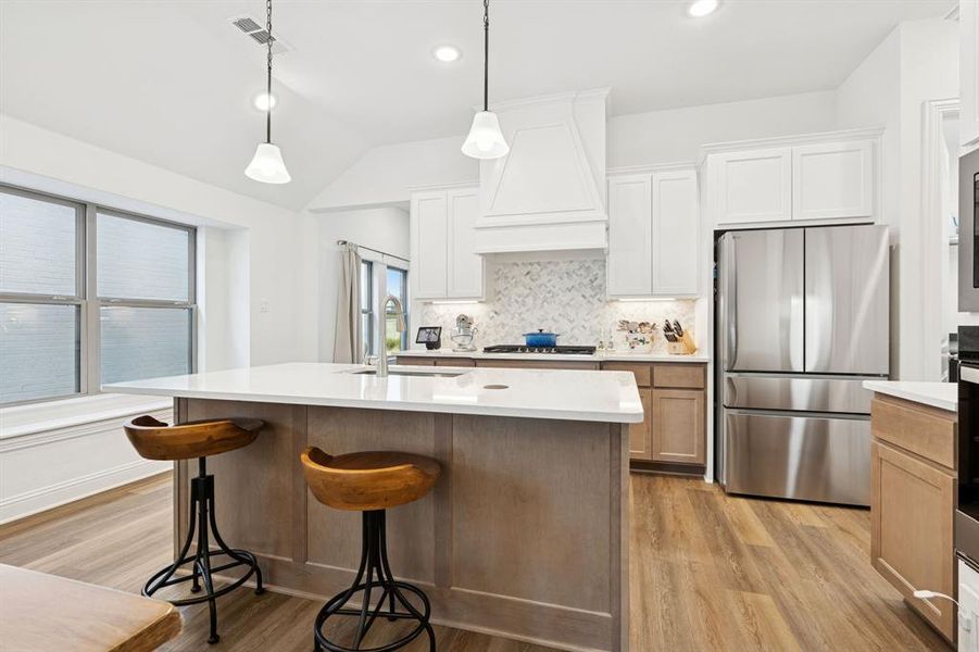 Kitchen featuring freestanding refrigerator, light wood-style flooring, decorative backsplash, brown cabinets, and white cabinets Kitchen featuring freestanding refrigerator, light wood-style flooring, decorative backsplash, brown cabinets, and white cabinets
