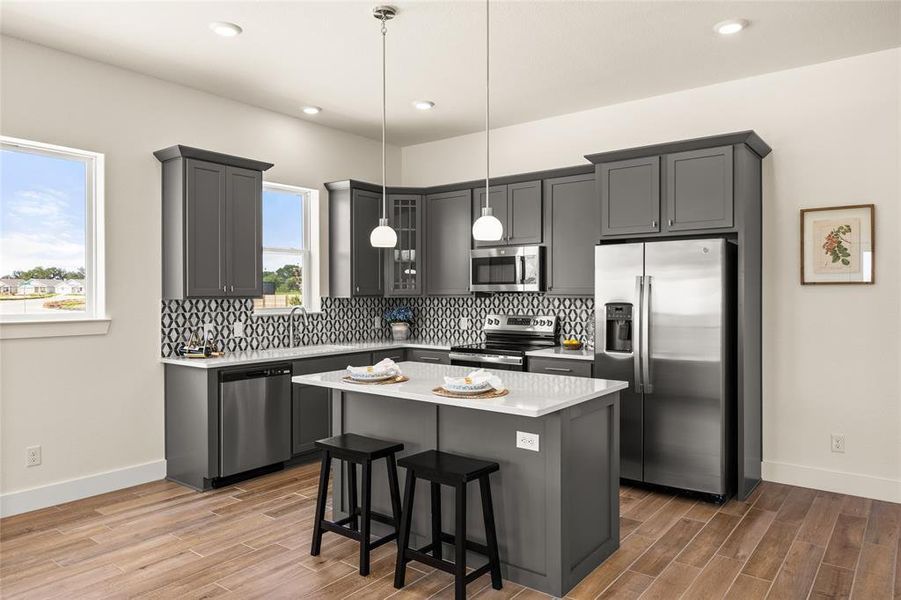 Modern kitchen featuring gray cabinetry, stainless steel appliances, a white island with seating, a patterned tile backsplash, and wood-finish flooring