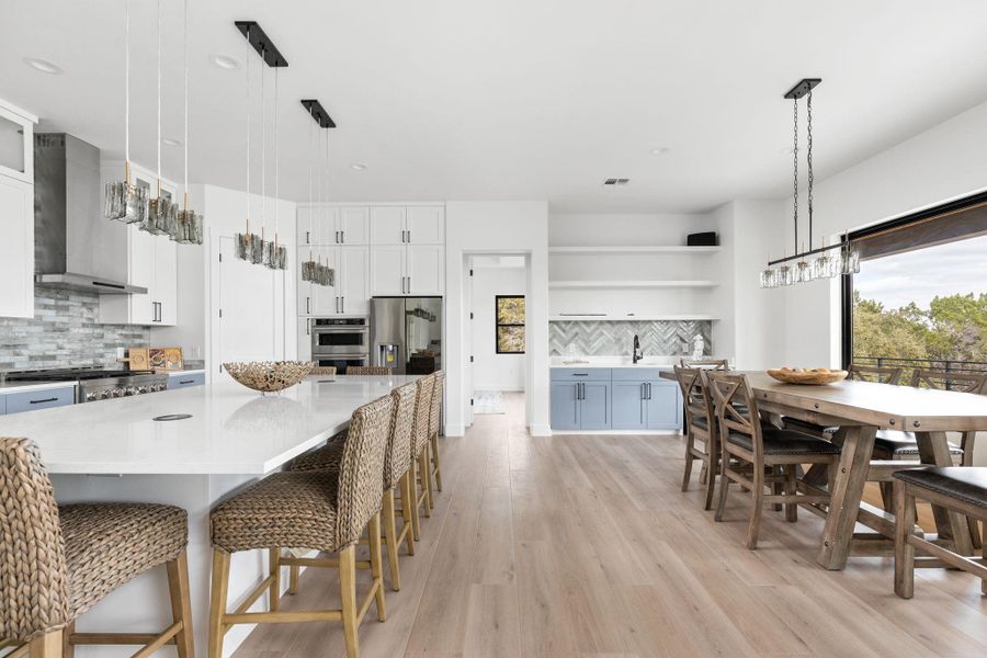 Kitchen featuring hanging light fixtures, backsplash, white cabinetry, wall chimney exhaust hood, and a breakfast bar