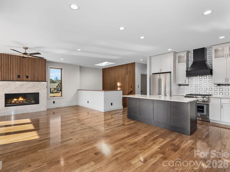 Representative photo from 50 Verde Drive showing the builder’s quality of construction and finish level, including the open-concept main living area, designer kitchen with center island, vented gas fireplace, and access to the stairwell, hall, and elevator.