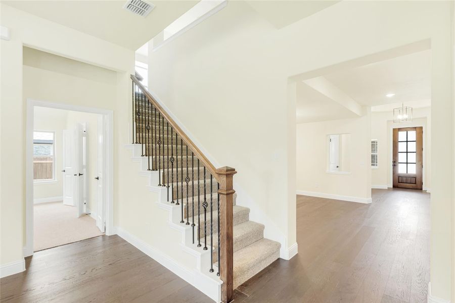 Carpeted staircase with wood handrail and iron balusters in an open entryway with dark hardwood floors Carpeted staircase with wood handrail and iron balusters in an open entryway with dark hardwood floors