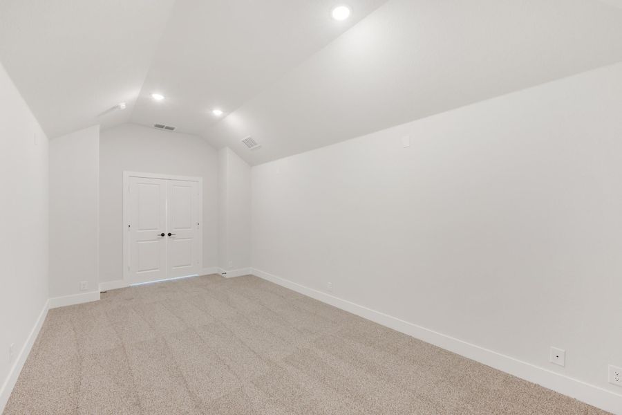 Empty bedroom with vaulted ceiling, recessed lighting, beige carpet, and white double doors