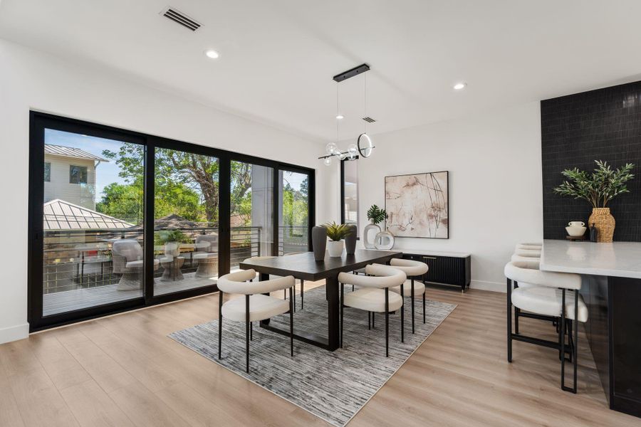 The sliding glass doors bring the covered balcony into the daily rhythm of the dining room — open them and the space extends outdoors without a step change. The adjacent kitchen island keeps the cook in the conversation from every angle.