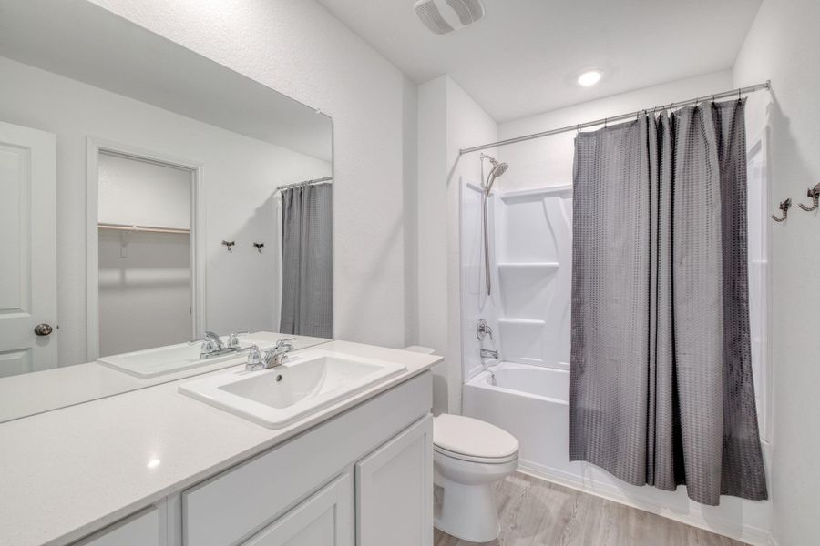 Contemporary bathroom featuring a white vanity with integrated sink, a large wall-mounted mirror, white bathtub with a shower kit, and light wood-finish flooring