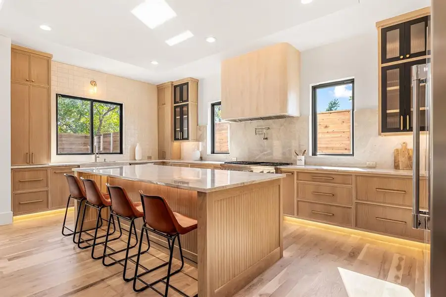 Kitchen featuring glass insert cabinets, light brown cabinets, a breakfast bar area, light stone countertops, and recessed lighting Kitchen featuring glass insert cabinets, light brown cabinets, a breakfast bar area, light stone countertops, and recessed lighting