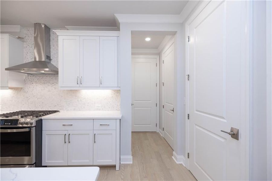 Kitchen with white cabinets, decorative backsplash, gas range, wall chimney range hood, and light hardwood / wood-style flooring