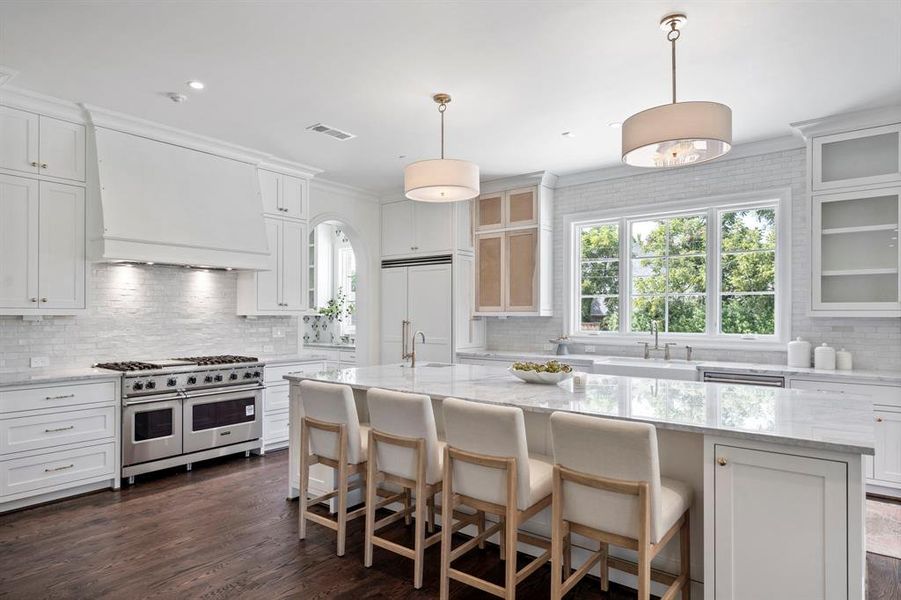 Kitchen featuring high end appliances, custom range hood, a center island with sink, and backsplash