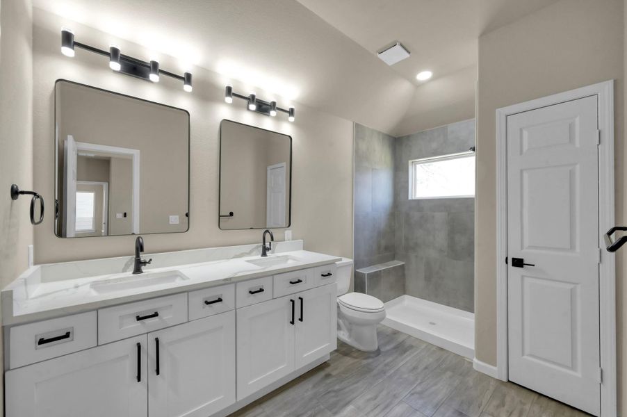 Step into luxury with this expansive primary vanity featuring dual sinks, pristine white cabinetry with modern black hardware, and elegant marbled quartz countertops. The twin statement mirrors and contemporary multi-bulb lighting create a bright, spa-like atmosphere.