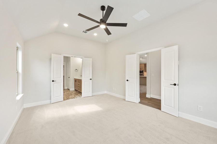 Empty master bedroom with carpet, ceiling fan, and doors leading to ensuite bathroom and hallway