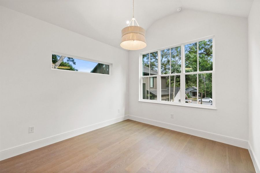 Natural light floods this versatile room, offering rich wood flooring and vaulted ceilings.
