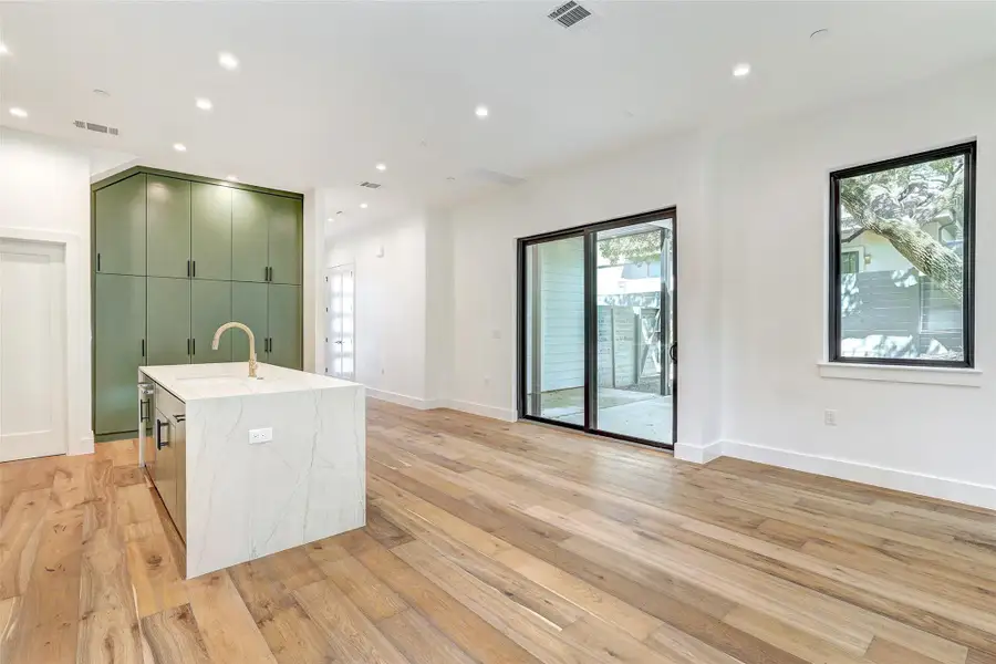 Kitchen with green cabinets, a sink, light wood-style floors, a center island with sink, and baseboards