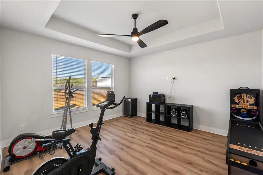Exercise room with a tray ceiling, light wood-style flooring, and ceiling fan