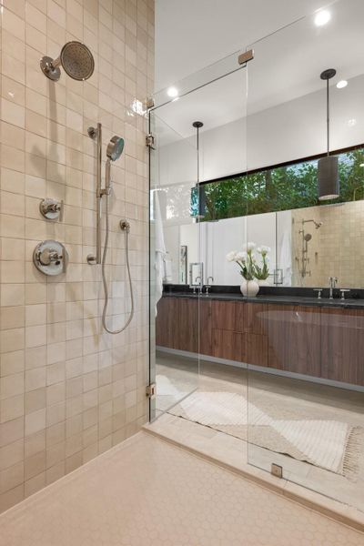 A spacious, naturally illuminated shower with modern fixtures complements the adjacent dual vanity with rich wood cabinetry. A spacious, naturally illuminated shower with modern fixtures complements the adjacent dual vanity with rich wood cabinetry.