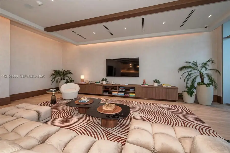 Living area featuring a recessed tray ceiling with integrated cove lighting, linear recessed lighting, wood-finish flooring, and a floor-to-ceiling built-in wooden media console