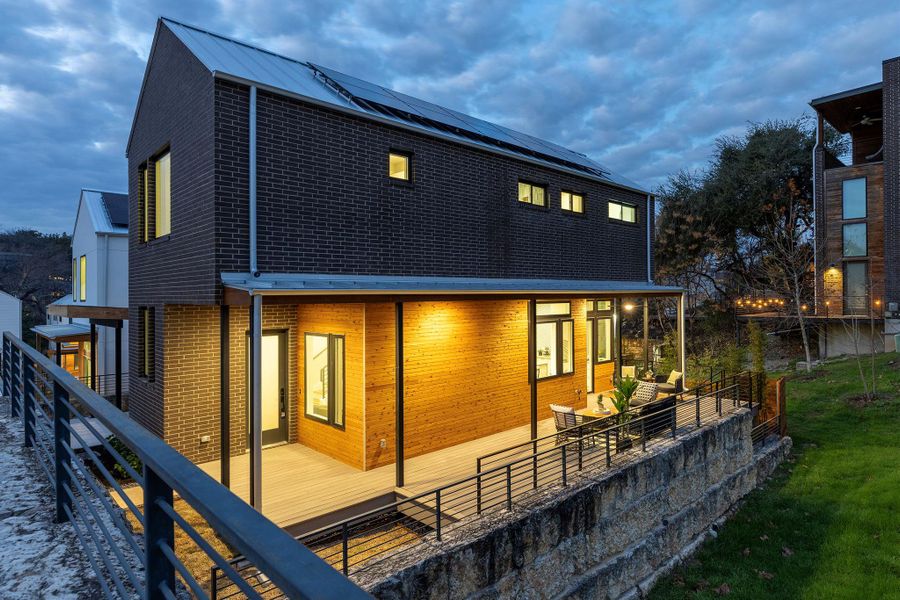 Rear view of house with roof mounted solar panels, fence, and brick siding