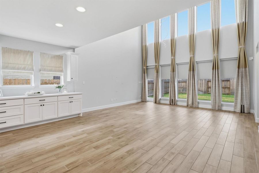 The dramatic two-story family room showcases soaring ceilings, a breathtaking wall of windows, and an abundance of natural light. This expansive space offers endless possibilities for furniture placement while creating the perfect setting for both everyday living and entertaining.