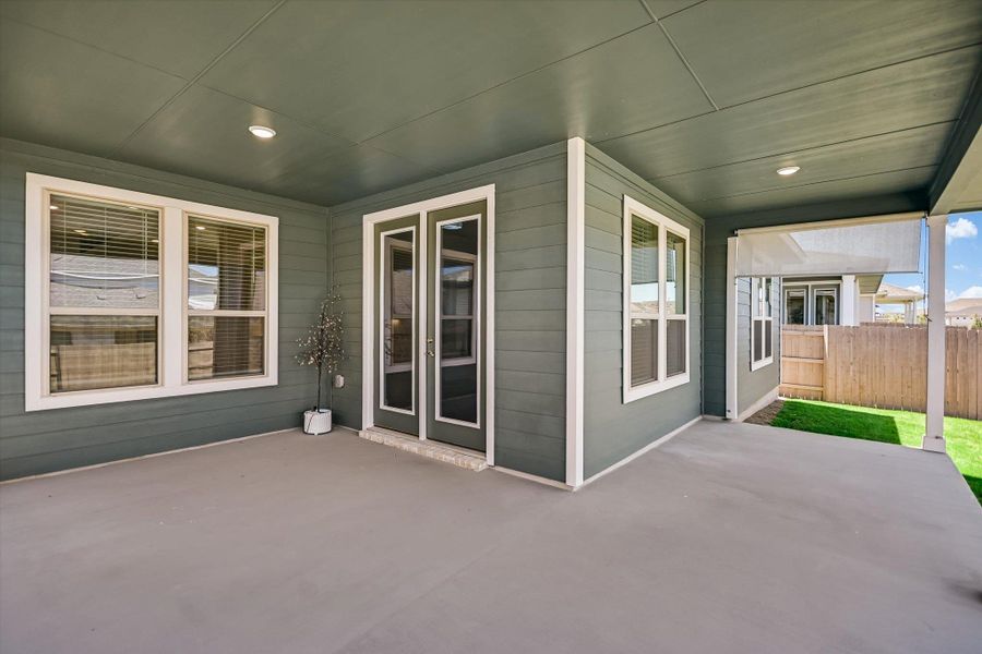 A covered concrete patio sits adjacent to the lawn with durable siding and classic glass doors. A covered concrete patio sits adjacent to the lawn with durable siding and classic glass doors.