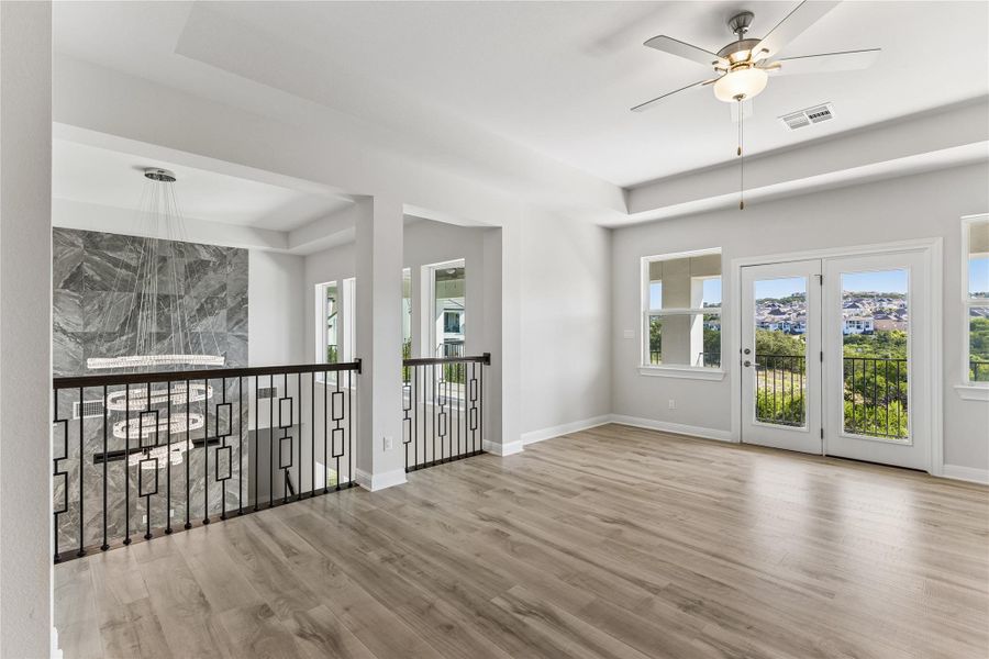 A well-lit upper-level space showcases durable hardwood flooring and a stylish ceiling fan, with a balcony offering expansive neighborhood views.