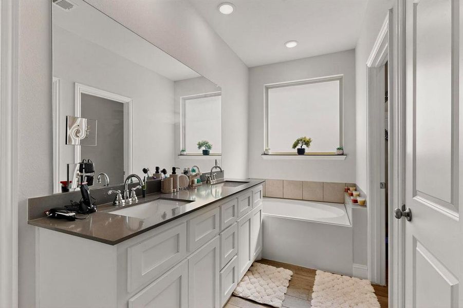 Full bath featuring double vanity, a bath, and light wood-type flooring Full bath featuring double vanity, a bath, and light wood-type flooring