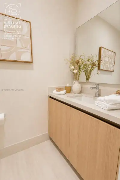 Floating vanity with light wood-finish cabinetry, stone-style countertop, integrated sink, chrome faucet, and expansive frameless wall mirror