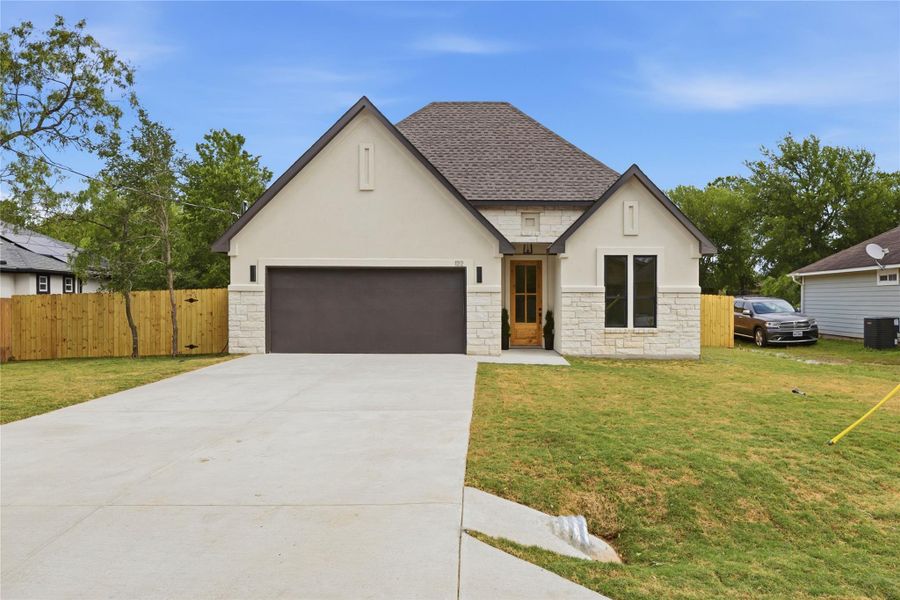 View of front facade featuring stone siding, stucco siding, driveway, roof with shingles, and an attached garage