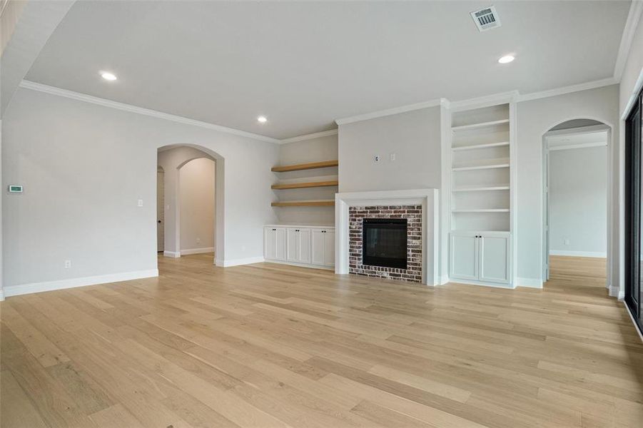 Unfurnished living room featuring built in features, a fireplace, light wood-type flooring, and ornamental molding