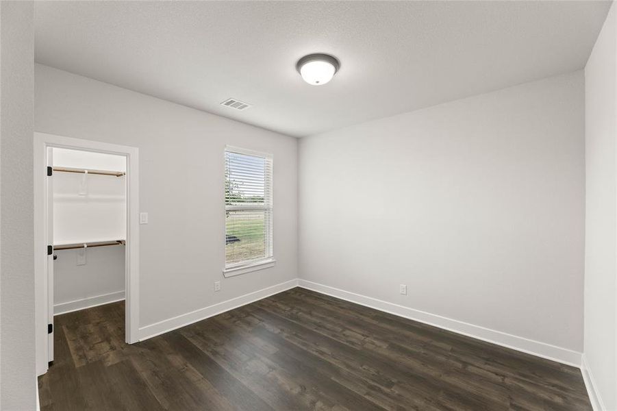 Unfurnished bedroom featuring dark wood finished floors and a spacious closet Unfurnished bedroom featuring dark wood finished floors and a spacious closet