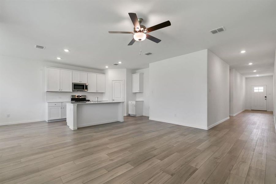 Kitchen with appliances with stainless steel finishes, ceiling fan, light wood-type flooring, white cabinetry, and a kitchen island with sink