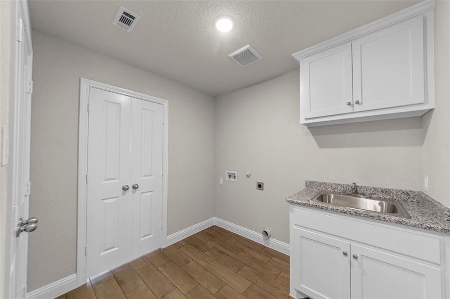 Dedicated utility space featuring wood-finish flooring, white cabinetry, a stainless steel sink with a granite countertop, and bi-fold doors