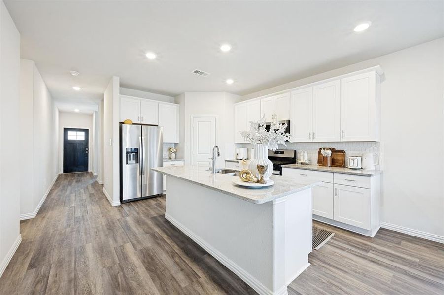 Modern kitchen featuring white cabinetry, light-toned countertops, stainless steel appliances, and a central island with an integrated sink Modern kitchen featuring white cabinetry, light-toned countertops, stainless steel appliances, and a central island with an integrated sink