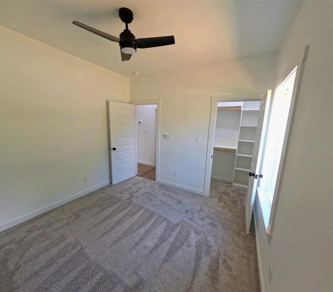 Unfurnished bedroom with a walk in closet, carpet, and a ceiling fan Unfurnished bedroom with a walk in closet, carpet, and a ceiling fan