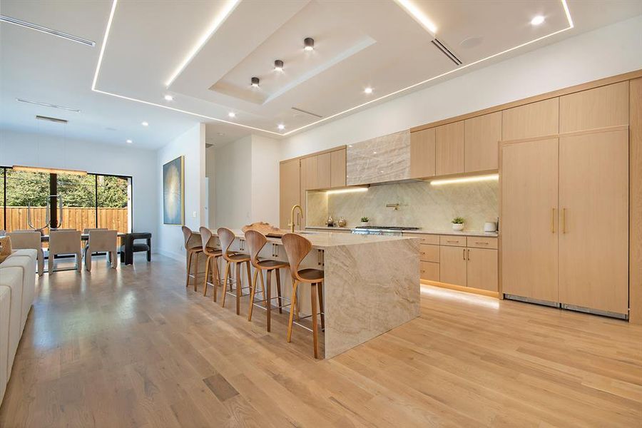 Kitchen with light brown cabinetry, light stone counters, decorative backsplash, a breakfast bar, and a large island with sink