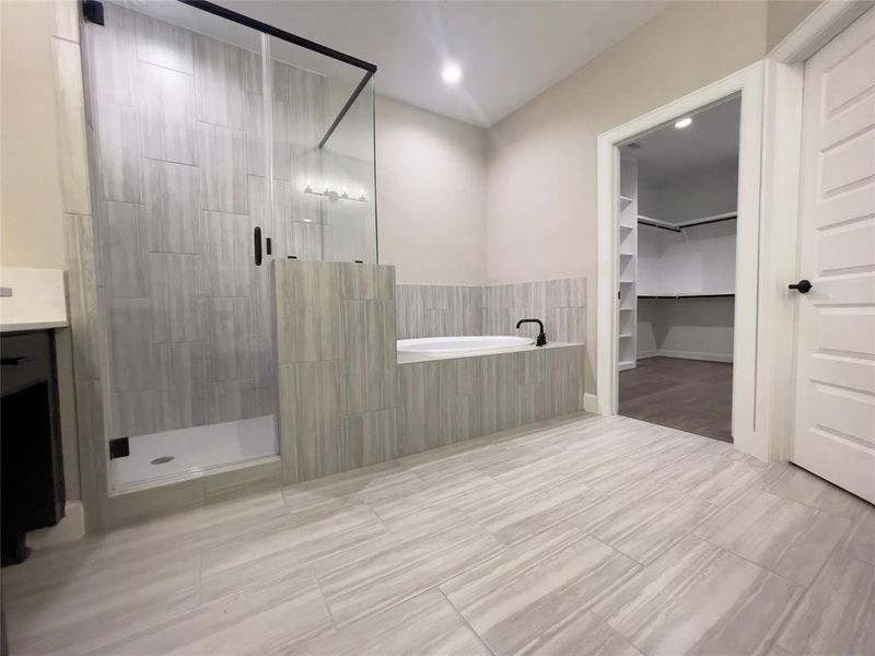 The ROClake's primary bathroom features a large shower and bathtub and dual vanities. The bright lighting fixtures and clean lines contribute to a serene, spa-like atmosphere. Image depicts home as is.